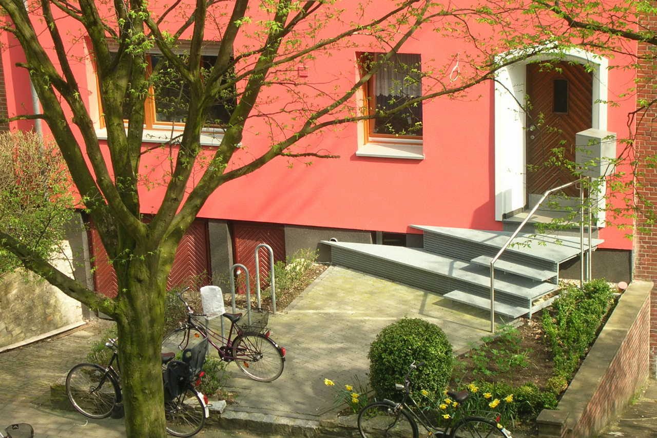Rot verputztes Mehrfamilienhaus mit neuem Eingang und Garten