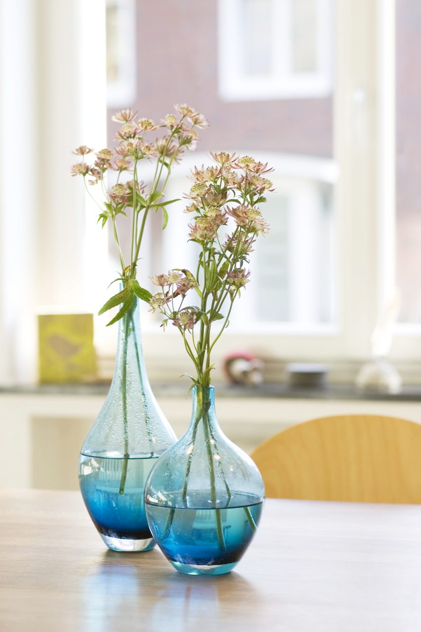 Zwei blaue Glasvasen mit Blumen in einem hellen, sanierten Wohnraum